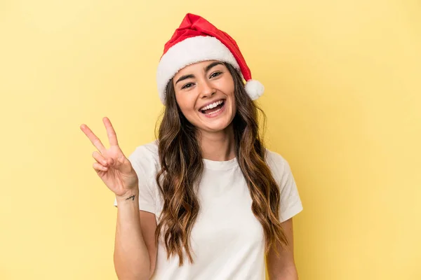 黄色の背景に孤立したクリスマスを祝う若い白人女性喜びと屈託のない指で平和のシンボルを示す — ストック写真