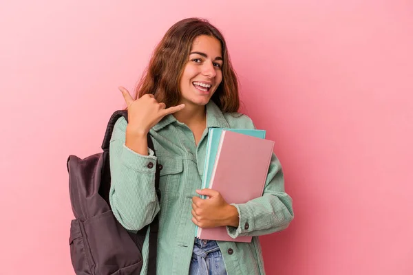 若いです白人学生女性保持本ピンクの背景に隔離された指で携帯電話の呼び出しジェスチャーを示しています — ストック写真