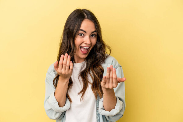 Young caucasian woman isolated on yellow background pointing with finger at you as if inviting come closer.