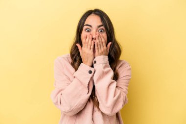 Sarı arka planda izole edilmiş genç beyaz kadın şok olmuş, ağzı ellerle kaplanmış, yeni bir şey keşfetmeye hevesli..