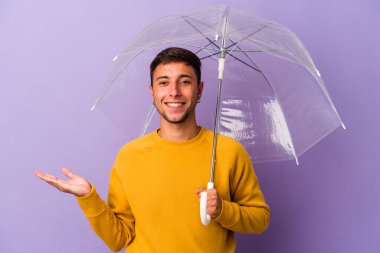 Mor arka planda şemsiyesi olan genç beyaz bir adam bir avuç içinde fotokopi alanı ve belinde başka bir el tutuyor..