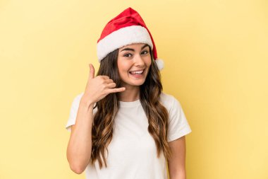 Sarı arka planda izole edilmiş bir şekilde Noel 'i kutlayan beyaz bir kadın cep telefonu hareketini parmaklarıyla gösteriyor..