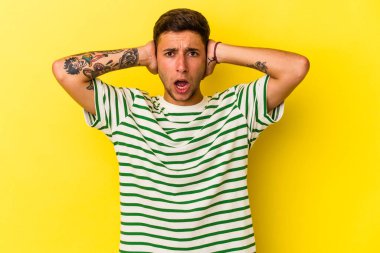 Sarı arka planda izole edilmiş dövmeleri olan genç beyaz bir adam kulaklarını elleriyle kapatıyor ve çok fazla ses duymamaya çalışıyor..