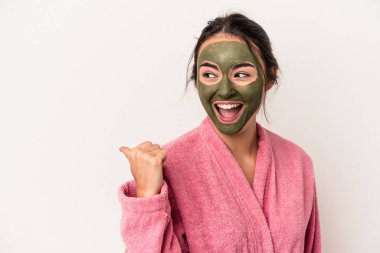Young caucasian woman wearing a facial mask isolated on white background points with thumb finger away, laughing and carefree.