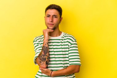 Sarı arka planda izole edilmiş dövmeleri olan beyaz bir genç şüpheli, belirsiz, seni muayene ediyor..