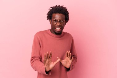 Genç Afro-Amerikalı bir adam pembe arka planda izole edilmiş, tiksinti belirtisi gösteren birini reddediyor..