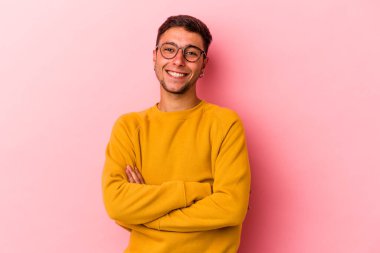 Sarı arka planda kendini güvende hisseden, kararlılıkla kollarını kavuşturan dövmeli beyaz bir genç..