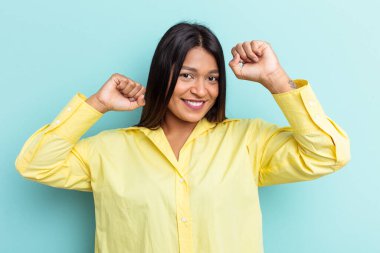 Genç Venezuelalı bir kadın mavi arka planda izole edilmiş özel bir günü kutluyor, atlıyor ve enerji ile kollarını kaldırıyor..