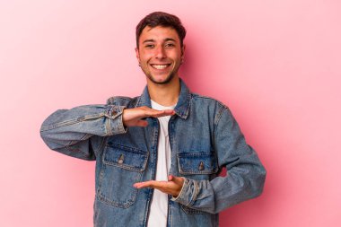 Sarı arka planda dövmeleri olan beyaz bir adam iki eliyle bir şey tutuyor, ürün sunumu..