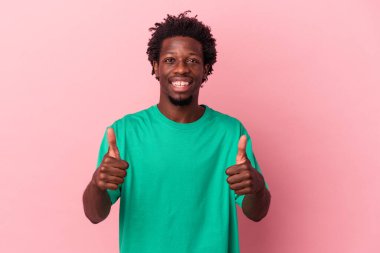 Genç Afrikalı Amerikalı adam pembe arka planda izole edilmiş gülümsüyor ve başparmağını kaldırıyor.