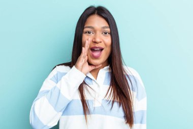 Genç Venezuelalı bir kadın mavi arka planda izole edilmiş yüksek sesle bağırıyor, gözlerini açık ve ellerini gergin tutuyor.