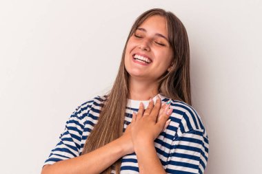 Beyaz arka planda soyutlanmış beyaz tenli genç bir kadın gülüyor, ellerini kalbe koyuyor, mutluluk kavramını koruyor..