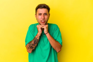 Sarı arka planda izole edilmiş beyaz dövmeli genç bir adam şans için dua ediyor, şaşırıyor ve ağzını açıyor..