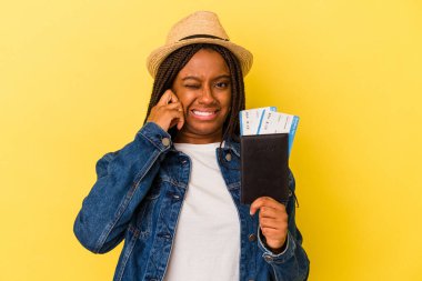 Pasaportu olan Afrikalı genç bir Amerikalı kadın sarı arka planda izole edilmiş kulakları elleriyle kapatıyor..