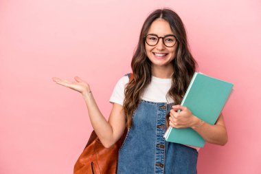 Young caucasian student woman isolated on pink background showing a copy space on a palm and holding another hand on waist.