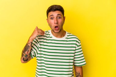 Sarı arka planda izole edilmiş dövmeleri olan genç beyaz bir adam bir şeye gülüyor, elleri ağızda..