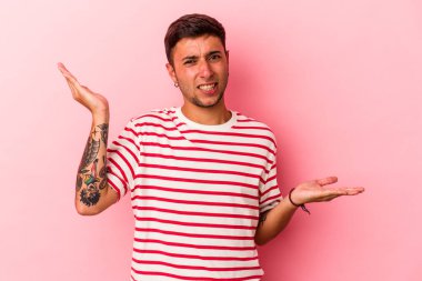 Sarı arka planda izole edilmiş beyaz dövmeli genç bir adam. Kafası karışmış ve omuz silkiyor..