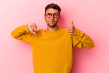 Sarı arka planda izole edilmiş beyaz dövmeli genç bir adam. Baş parmağını kaldırıyor ve baş parmağıyla işaret ediyor. Zor bir seçim.