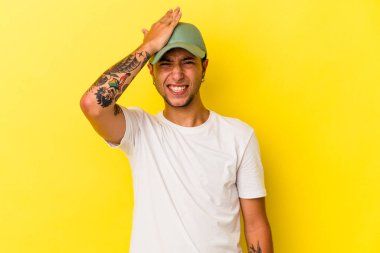 Sarı arka planda izole edilmiş dövmeleri olan genç beyaz bir adam bir şeyi unutuyor. Alnına avuç içi ve kapalı gözlerle tokat atıyor..