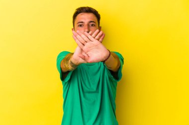 Sarı arka planda dövmeleri olan beyaz bir adam inkar hareketi yapıyor.