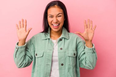 Pembe arka planda izole edilmiş genç Latin kadın hoş bir sürpriz alıyor, heyecanlı ve el kaldırıyor..