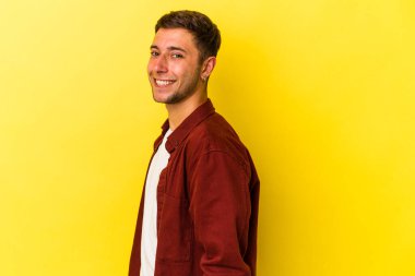 Sarı arka planda izole edilmiş dövmeleri olan genç, beyaz bir adam ellerini kalçasında tutuyor..