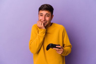 Mor arka planda izole edilmiş, tırnak yiyen, gergin ve endişeli bir oyun kumandanı tutan genç beyaz adam..