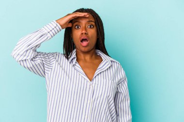 Genç Afrikalı Amerikalı kadın mavi arka planda izole edilmiş, uzaklara bakıyor ve elini alnına koyuyor..