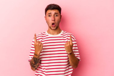 Sarı arka planda izole edilmiş, ağzı açık, üst tarafı işaret eden dövmeleri olan beyaz bir genç..