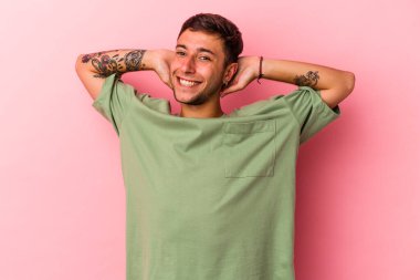 Sarı arka planda izole edilmiş, kollarını esneten, rahat bir pozisyonda dövmeleri olan genç beyaz bir adam..