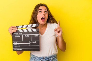 Sarı arka planda elinde klaket tutan beyaz bir kadın ağzı açık bir şekilde üst tarafı işaret ediyor..