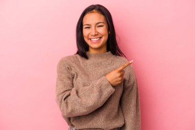 Pembe arka planda izole edilmiş genç Latin kadın gülümsüyor ve boş alanda bir şeyler gösteriyor..