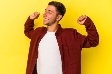 Sarı arka planda izole edilmiş, kollarını esneten, rahat bir pozisyonda dövmeleri olan genç beyaz bir adam..