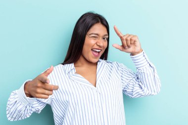 Genç Venezuelalı bir kadın mavi arka planda izole edilmiş, parmaklarıyla ön tarafı işaret ediyor..