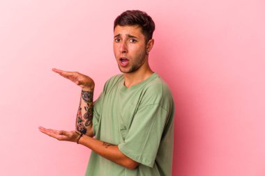 Sarı arka planda izole edilmiş beyaz dövmeli genç bir adam elleri arasında bir kopya alanı tutarken şok ve hayrete düştü..