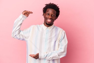 Genç Afrikalı Amerikalı bir adam pembe arka planda izole edilmiş. Elinde parmakları olan, gülümseyen ve kendinden emin bir şey var..