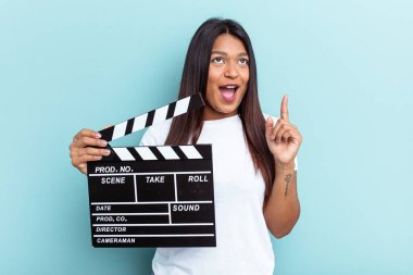 Genç Venezüellalı bir kadın mavi arka planda izole edilmiş bir alçıpan tutuyor ve ağzı açık bir şekilde yukarı bakıyor..