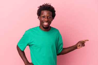 Pembe arka planda izole edilmiş genç Afro-Amerikalı adam mutlu bir şekilde işaret parmağıyla işaret ediyor..