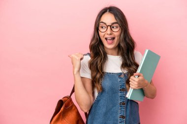Young caucasian student woman isolated on pink background points with thumb finger away, laughing and carefree.
