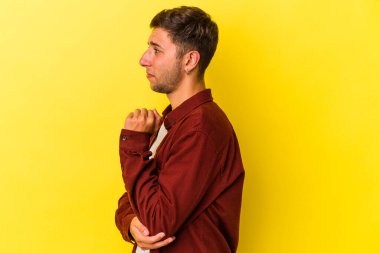 Sarı arka planda izole edilmiş dövmeleri olan genç beyaz adam kafası karışmış, şüpheli ve güvensiz hissediyor..