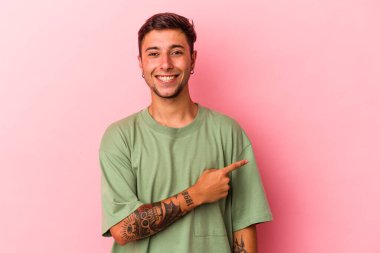 Sarı arka planda izole edilmiş, gülümseyen ve işaret eden, boş alanda bir şeyler gösteren beyaz dövmeli genç bir adam..