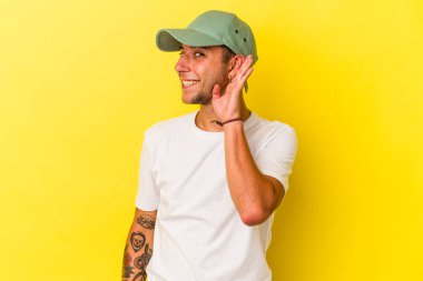 Sarı arka planda izole edilmiş dövmeleri olan beyaz bir adam bir dedikoduyu dinlemeye çalışıyor..