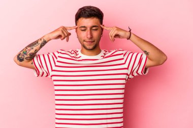 Sarı arka planda izole edilmiş dövmeleri olan beyaz genç bir adam görevine odaklanmış, işaret parmaklarını işaret ediyor..