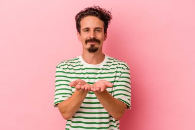 Pembe arka planda izole edilmiş genç beyaz bir adam elinde avuç içi bir şeyle kameraya sunuyor..