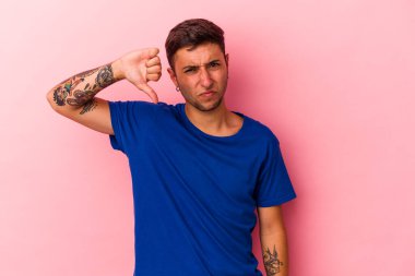 Sarı arka planda izole edilmiş dövmeleri olan genç beyaz bir adam baş parmağını aşağı gösteriyor ve hoşlanmadığını ifade ediyor..