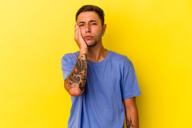Sarı arka planda izole edilmiş dövmeleri olan, üzgün ve dalgın hisseden, kopyalama alanına bakan genç beyaz bir adam..