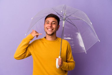 Mor arka planda şemsiyesi olan beyaz bir genç, parmakları olan bir cep telefonu hareketi gösteriyor..