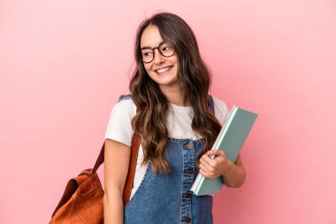 Young caucasian student woman isolated on pink background looks aside smiling, cheerful and pleasant.