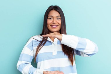 Genç Venezuelalı bir kadın mavi arka planda iki eliyle bir şey tutuyor, ürün sunumu..