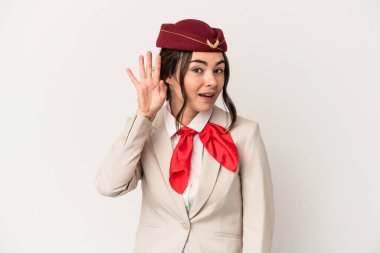 Young caucasian stewardess woman isolated on white background trying to listening a gossip.
